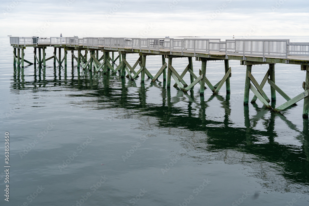 A view of the long pier and the Long Island Sound at Calf Pasture Beach in Norwalk, Connecticut USA on a cold and grey December day. The flat light lends a dreamy feel to the scene.