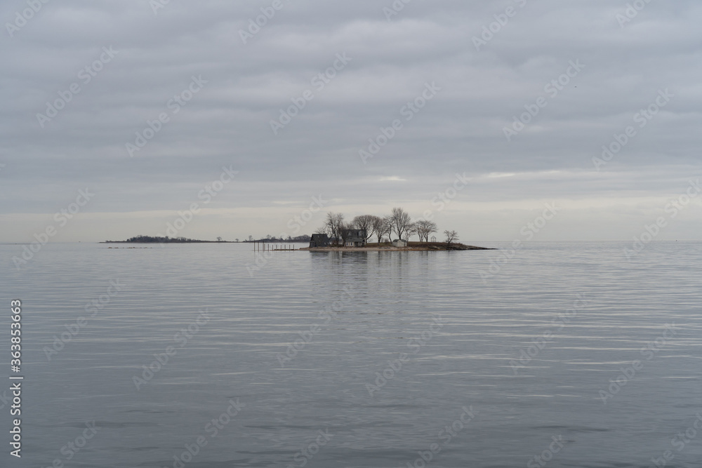A view from the pier across the Long Island Sound to a small island off Calf Pasture Beach in Norwalk, Connecticut USA on a cold and grey December day. The flat light lends a dreamy feel to the scene.