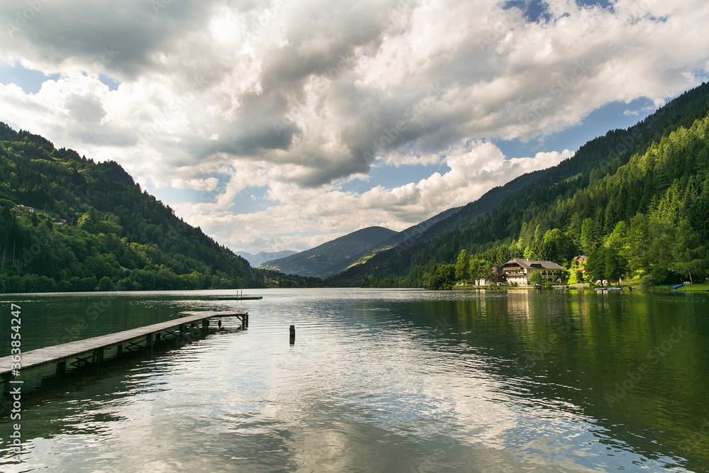 One walk along the promenade of the Austrian mountain lake. White clouds, green forest, dark blue water. One walk along the promenade of the Austrian mountain lake. White clouds, green forest, dark blue water.