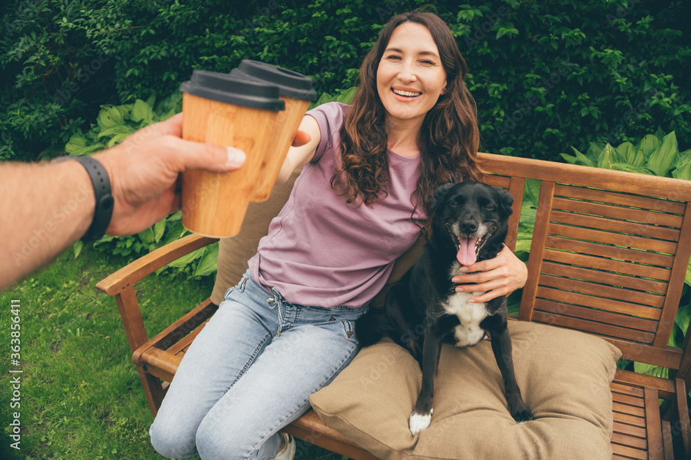 POV image of young couple toasting with bamboo coffee cups sitting in summer garden with dog - concept of happy family, sustainable living, plastic reduction and ecology POV image of young couple toasting with bamboo coffee cups sitting in summer garden with dog - concept of happy family, sustainable living, plastic reduction and ecology