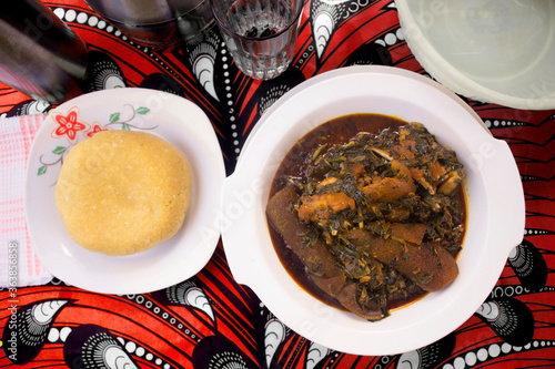 A delicious meal of Nigerian vegetable soup cooked with assorted meat, dried fish, cow skin (ponmo or kpomo or pomo) and Garri or Eba. Served on a colorful red and white African pattern table cloth photo