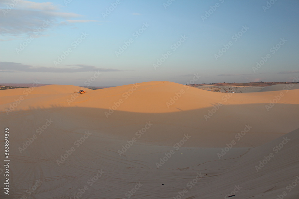 mound in the desert in the morning has a sky background and there is a car running in the desert. There is sunshine in the morning.