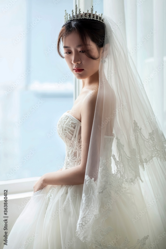 Asian women in white wedding dresses stand at the window waiting for the bridegroom's arrival, looking happy and happy Asian women in white wedding dresses stand at the window waiting for the bridegroom's arrival, looking happy and happy