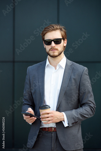 Well-dressed young businessman with phone and coffee looking at the camera photo