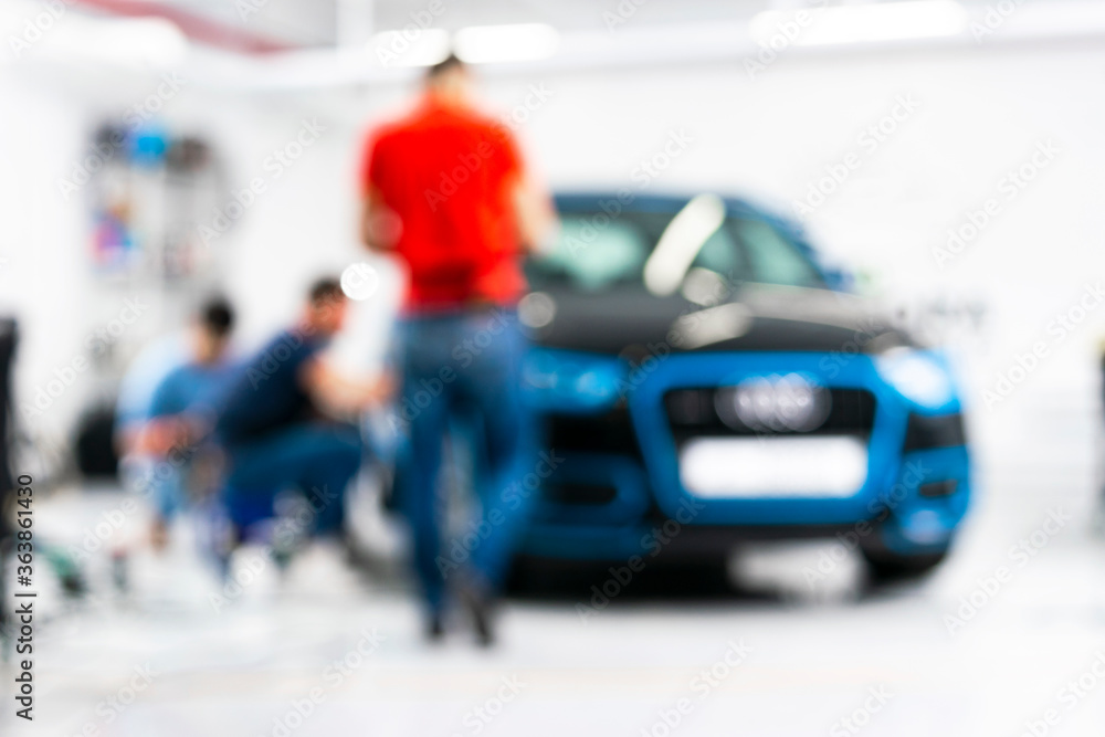 Fototapeta premium Blurred abstract image of man worker with car in a body shop. Blur car auto service. Car bokeh. Blurred background with car in garage. Vehicle maintenance in auto repair service. 
