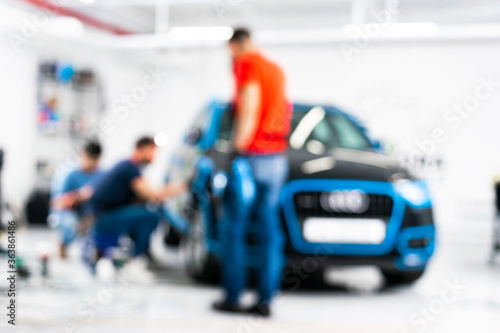 Blurred abstract image of man worker with car in a body shop. Blur car auto service. Car bokeh. Blurred background with car in garage. Vehicle maintenance in auto repair service. 