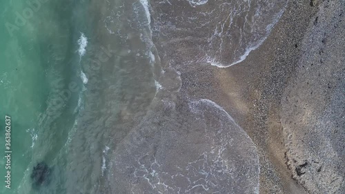 Overhead view of ocean waves washing onto coarse sandy beach.