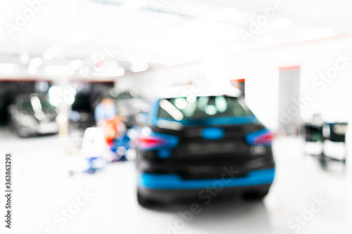 Blurred abstract image of man worker with car in body shop. Blur car auto service. Car bokeh. Blurred background with car in garage. Vehicle maintenance in auto repair service. Blurry service station © Aleksei