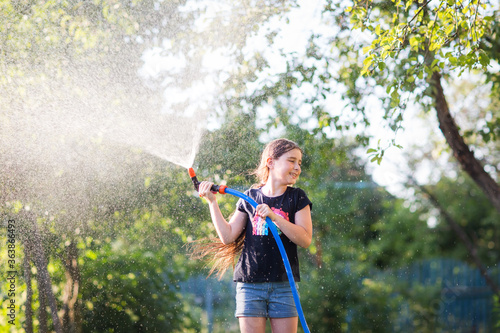 child uses hose to water plants in garden in Sunny hot summer day. kids fun. girl waters herself from shower. tool for pour
