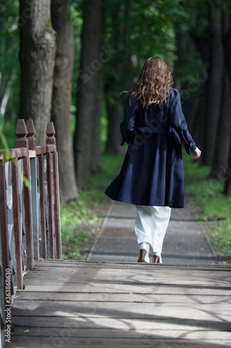  A girl with long hair walks on a wooden bridge in a summer Park. 