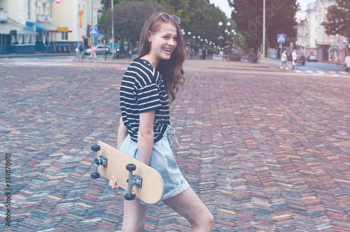 Beautiful smiling teenager girl with a skateboard in the city center, vintage and instagram tinted
