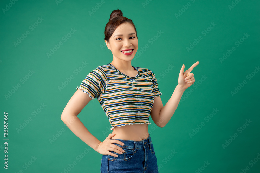 Happy young Asian woman in casual clothing pointing her finger over green background. Happy young Asian woman in casual clothing pointing her finger over green background.