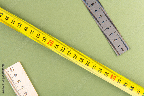 different rulers and measuring tape of builders are on the table; green background