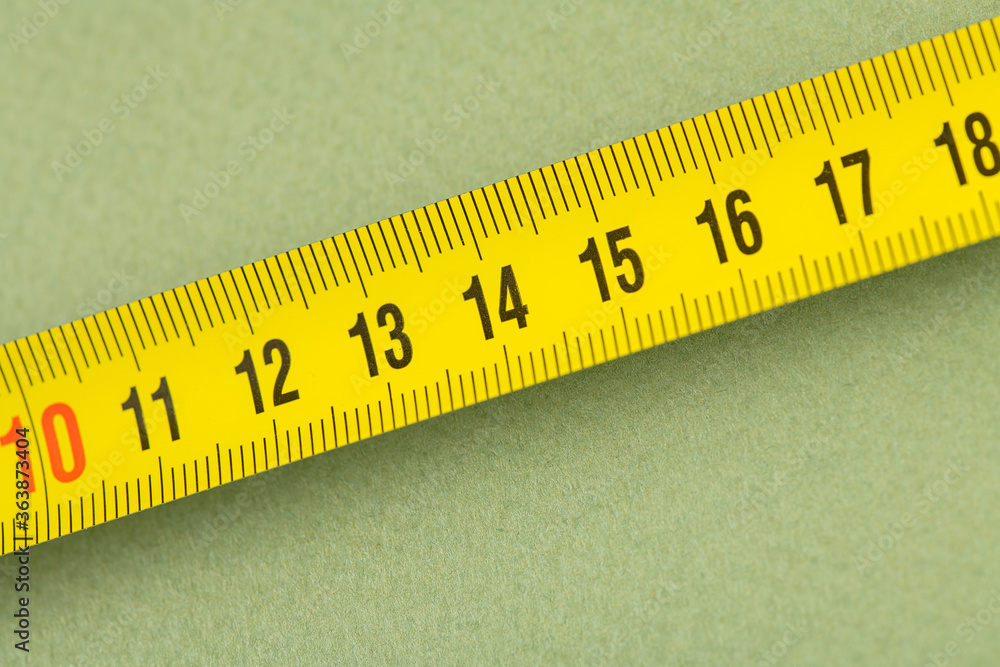 yellow construction measuring tape lies on a table, closeup photo 11 - 17 centimeters; green background yellow construction measuring tape lies on a table, closeup photo 11 - 17 centimeters; green background