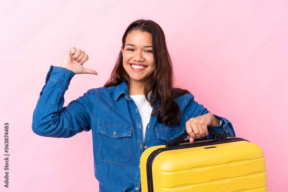 Traveler Colombian woman holding a suitcase over isolated pink background proud and self-satisfied