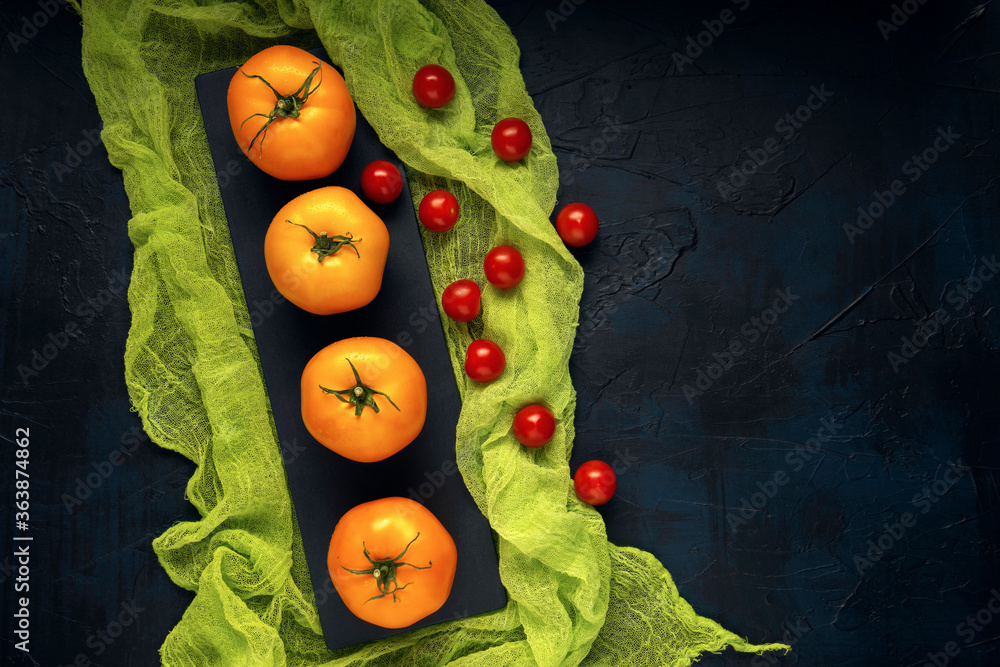 A few yellow tomato fruits with red cherry tomatoes on serving board with green gauze. Dark background. Vegetable composition. Space for text. Top view.