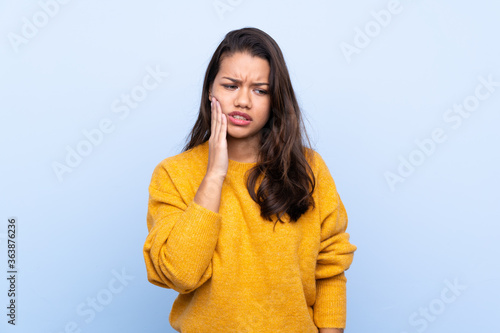 Young Colombian girl with sweater over isolated blue background with toothache