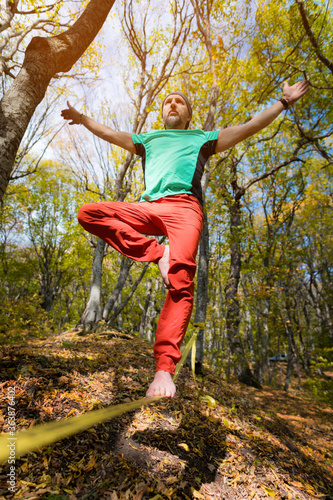 A bearded man aged walks along a slackline in the autumn forest on a sunny afternoon. The concept of Leisure and Recreation of active middle-aged people