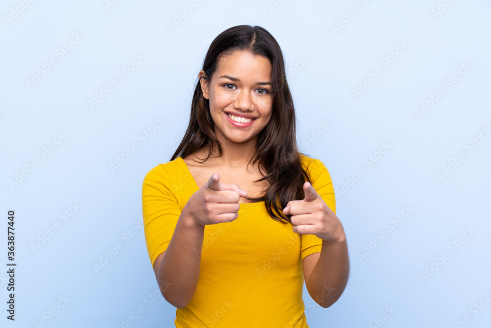 Young Colombian girl over isolated blue background points finger at you Young Colombian girl over isolated blue background points finger at you
