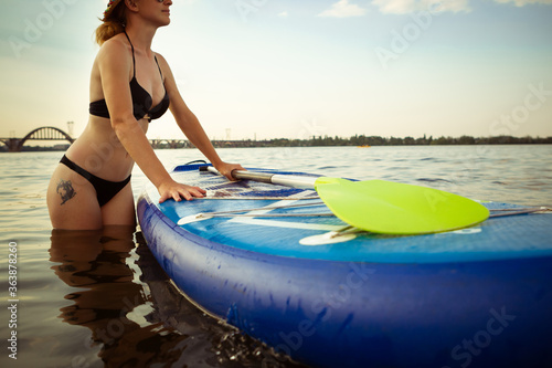 Time for enjoyment. Young attractive woman carries paddle board, SUP. Active life, sport, leisure activity concept. Caucasian woman on travel board in summers evening time. Vacation, resort, enjoyment