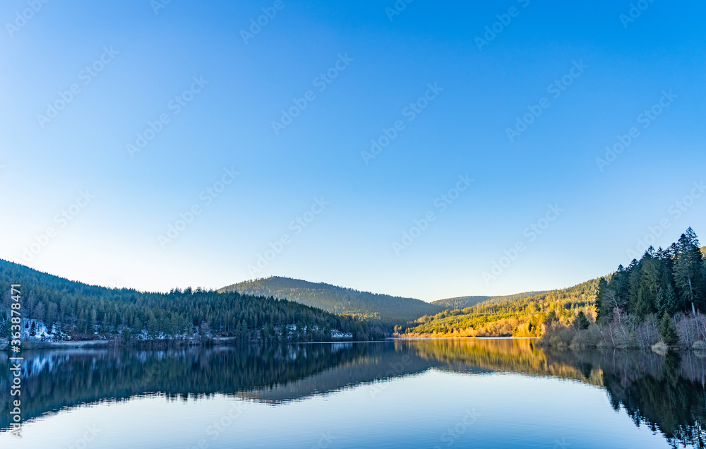 Mountains reflection on lake against clear blue sky in sunlight
