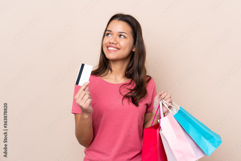 Young Colombian girl with shopping bag over isolated background holding shopping bags and a credit card