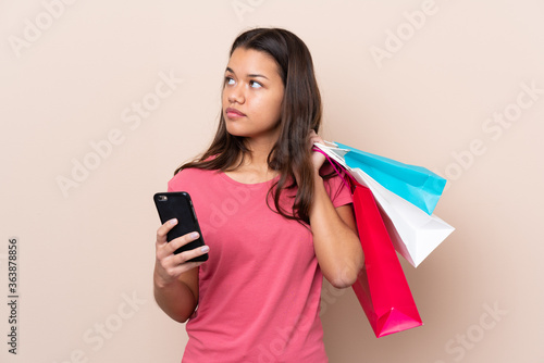 Young Colombian girl with shopping bag over isolated background holding shopping bags and a mobile phone