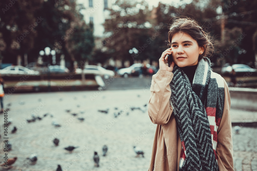 Pretty teen girl strolling on a square full of doves, talking on phone and enjoying the last warm days in a year. Pretty teen girl strolling on a square full of doves, talking on phone and enjoying the last warm days in a year.