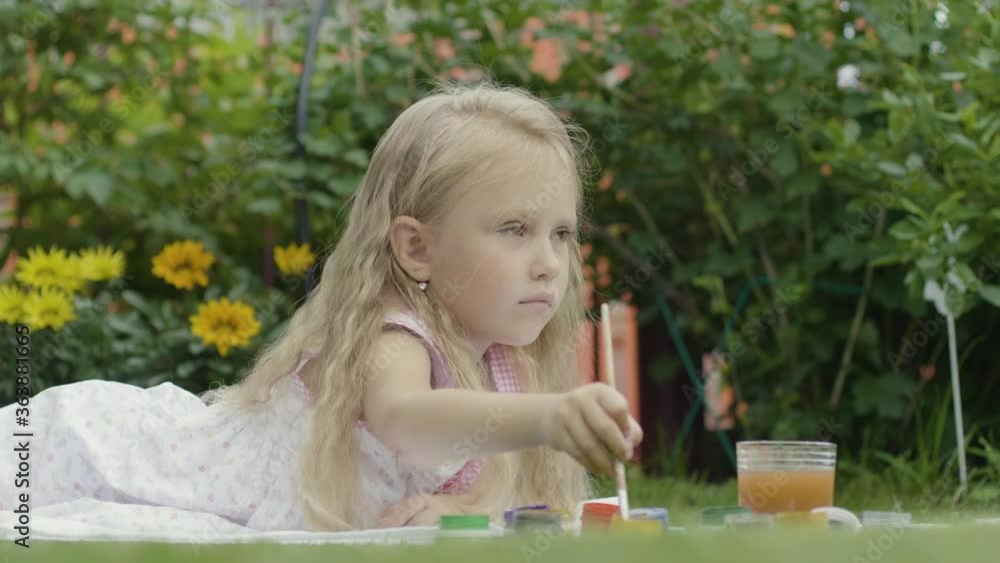 Blond girl draws paints on the nature. Girl 5 years old lies on the grass and paints a picture Blond girl draws paints on the nature. Girl 5 years old lies on the grass and paints a picture