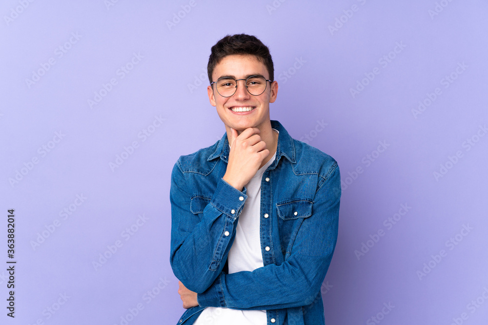 Teenager caucasian handsome man isolated on purple background with glasses and smiling Teenager caucasian handsome man isolated on purple background with glasses and smiling
