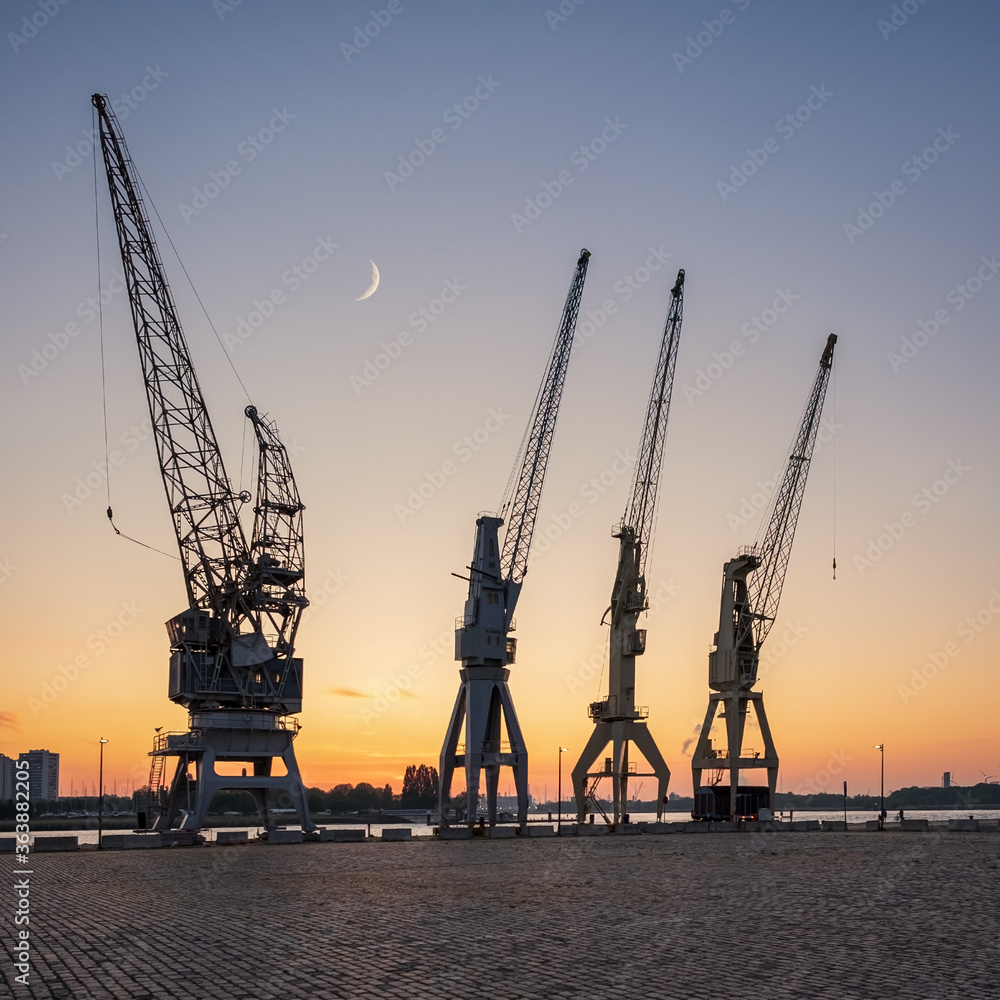 Old harbor crane silhouettes under a crescent moon. The cranes are part of the collection of the MAS museum.