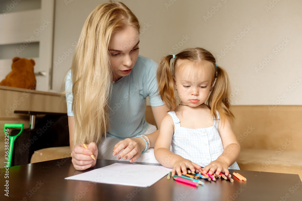 Young beautiful mother blonde and her daughter 2 years old draw with pencils on the sofa in the living room at home Young beautiful mother blonde and her daughter 2 years old draw with pencils on the sofa in the living room at home