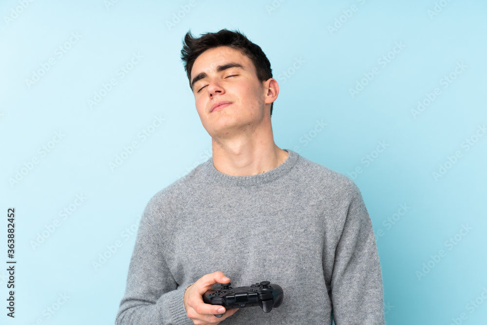 Teenager caucasian man playing with a video game controller isolated on blue background Teenager caucasian man playing with a video game controller isolated on blue background