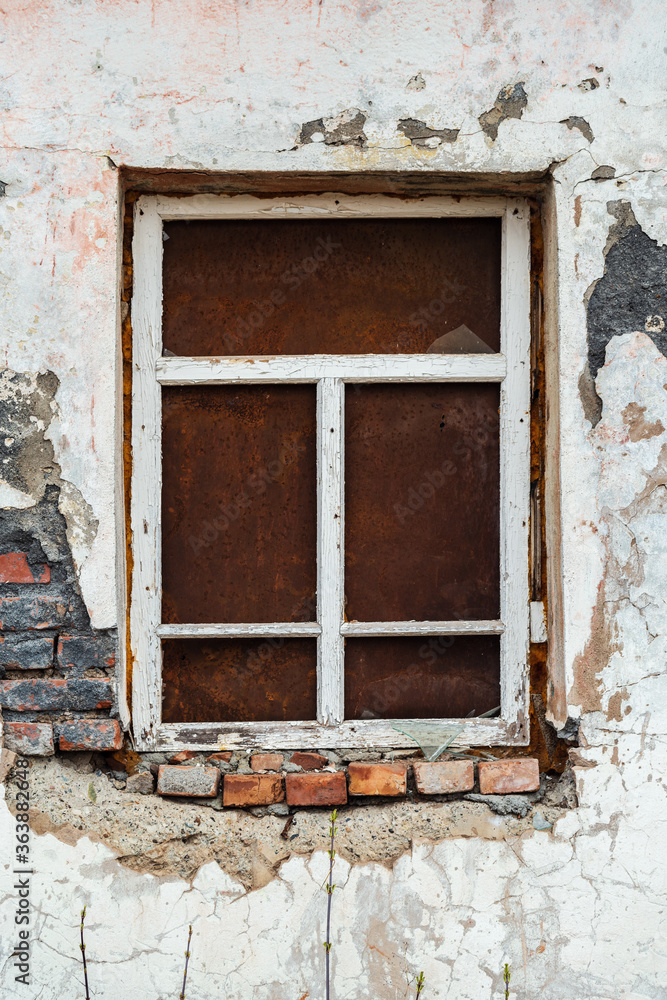 Fototapeta premium The ragged wall of an old abandoned building, with a window closed by a sheet of rusty metal. The picture was taken in Russia, in the Orenburg region, in the countryside