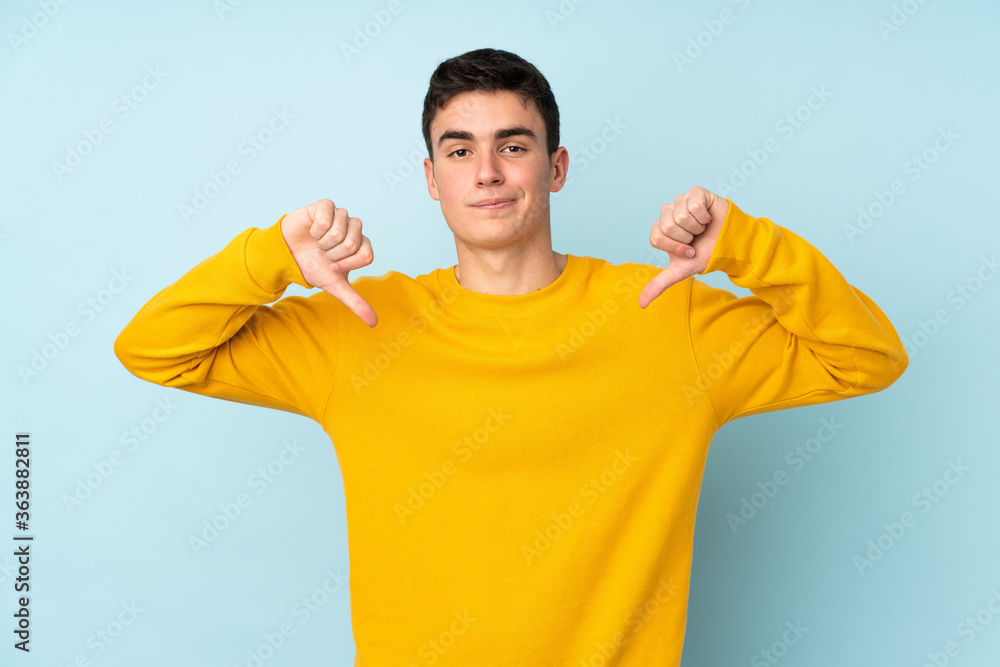 Teenager caucasian handsome man isolated on purple background showing thumb down Teenager caucasian handsome man isolated on purple background showing thumb down