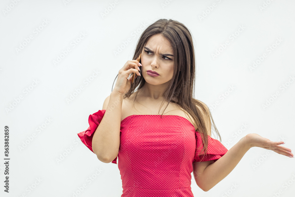Young brunette female frowning because of bad news while standing over over white background talking on the phone. Young brunette female frowning because of bad news while standing over over white background talking on the phone.