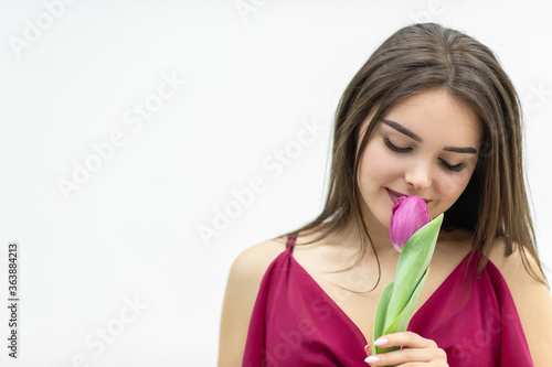 Beautiful girl in the maroon dress smells a tender tulip over white background.