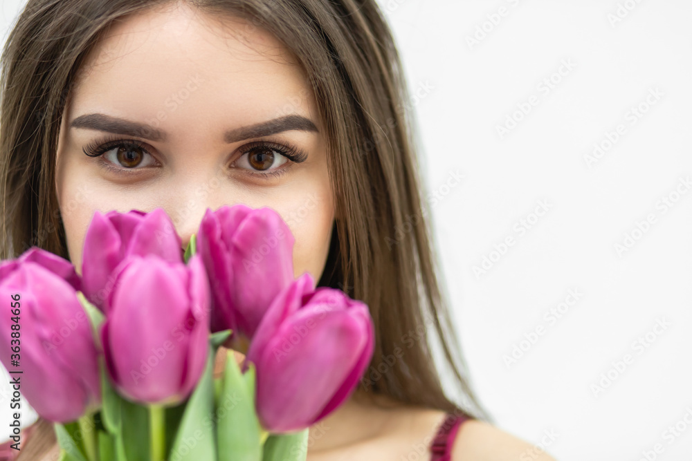 Cropped shot of young cute woman smelling pink tulip, slightly smiling at the camera, looking peacefull. Cropped shot of young cute woman smelling pink tulip, slightly smiling at the camera, looking peacefull.