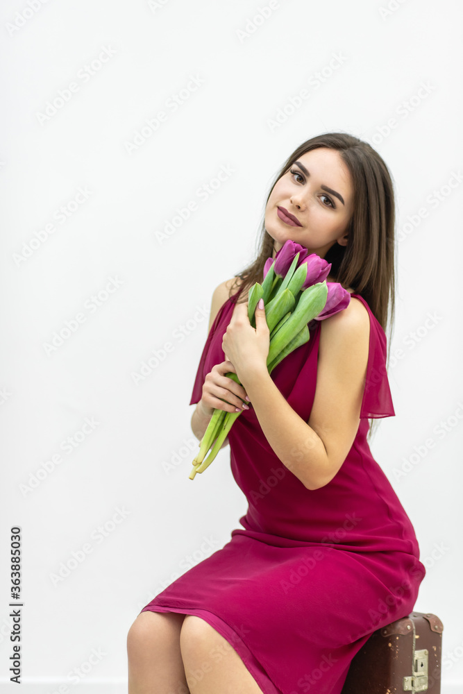 Happy Women's Day. Excited woman sits on the chair with a bunch of tulips on the occasion of spring female holiday. Happy Women's Day. Excited woman sits on the chair with a bunch of tulips on the occasion of spring female holiday.
