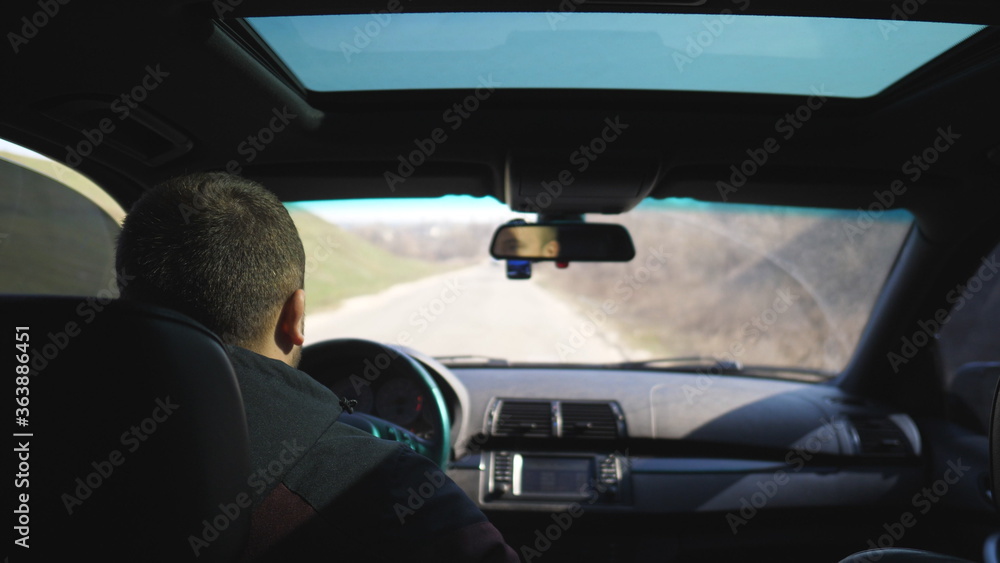 View from backseat on young man drives a car on empty road. Guy rides in his modern SUV through countryside. Male tourist travels on his auto. Concept of journey. Close up Slow motion