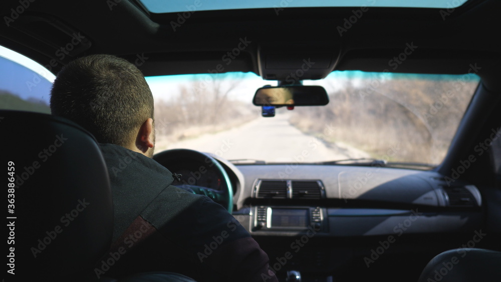 View from backseat on young man drives a car on empty road. Guy rides in his modern SUV through countryside. Male tourist travels on his auto. Concept of journey. Close up Slow motion