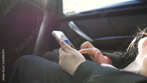 Female hands of small girl browses social media on smart phone during riding on modern SUV. Little child sits in backseat of moving car and types text message on her mobile phone. Slow motion