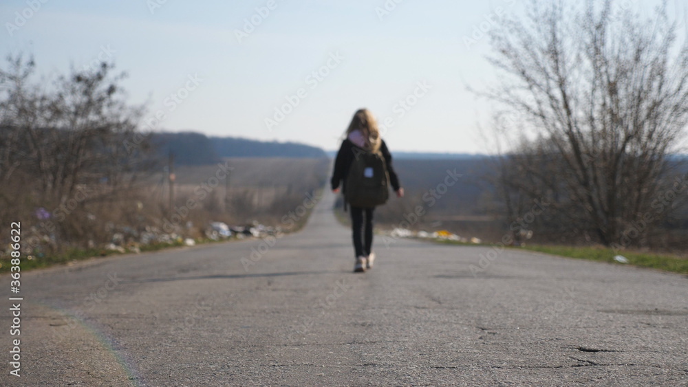 Small girl with backpack walks among road to training. Female child in jacket goes along a driveway to school. Unrecognizable little kid moves on way at sunny day. Blurred motion. Crane shot Slow mo