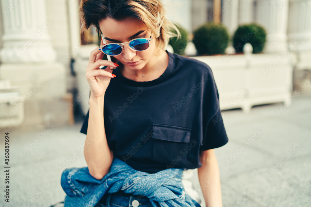 Stylish hipster girl in trendy sunglasses talking on mobile phone while strolling in street.Busy businesswoman dressed in black t-shirt communicating on modern smartphone device walking outdoors Stylish hipster girl in trendy sunglasses talking on mobile phone while strolling in street.Busy businesswoman dressed in black t-shirt communicating on modern smartphone device walking outdoors
