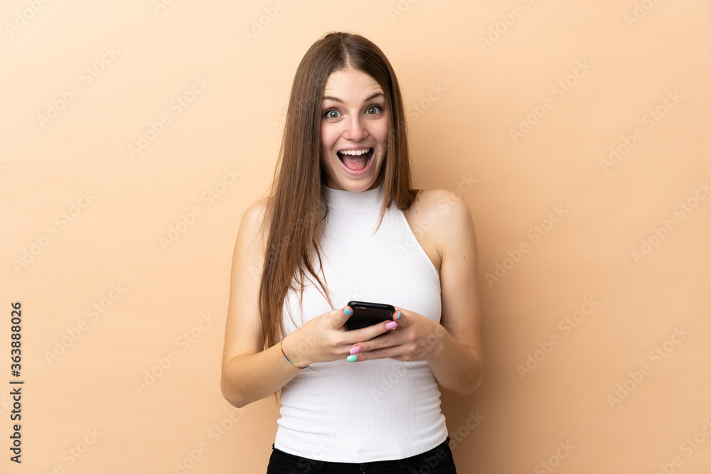 Young caucasian woman isolated on beige background surprised and sending a message Young caucasian woman isolated on beige background surprised and sending a message