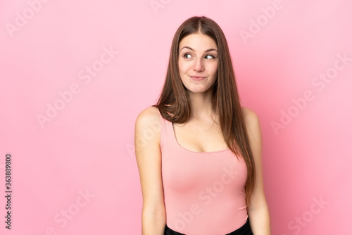 Young caucasian woman isolated on pink background making doubts gesture looking side