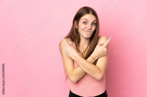 Young caucasian woman isolated on pink background pointing to the laterals having doubts