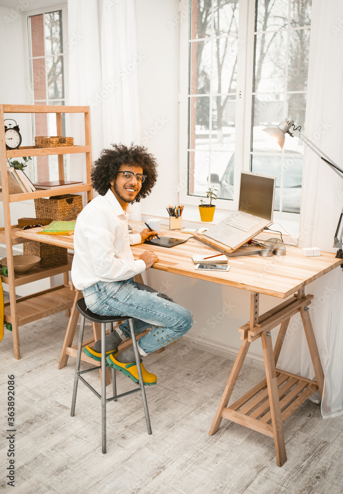 Workplace near window. Creative man looking at camera working with laptop at home office interior. Freelance concept. Tinted image.