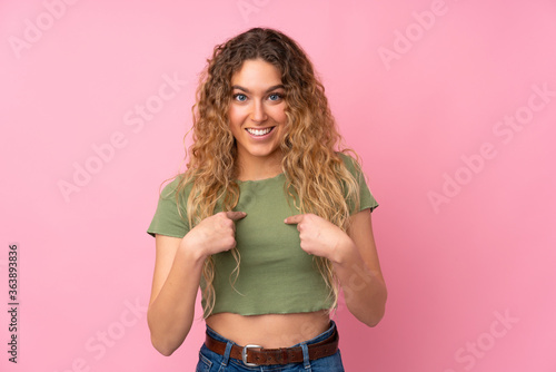 Young blonde woman with curly hair isolated on pink background with surprise facial expression