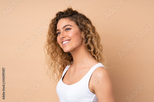 Young blonde woman with curly hair isolated on beige background . Portrait